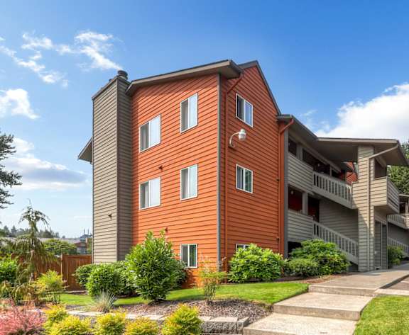 A red car is parked in front of a two-story apartment building.