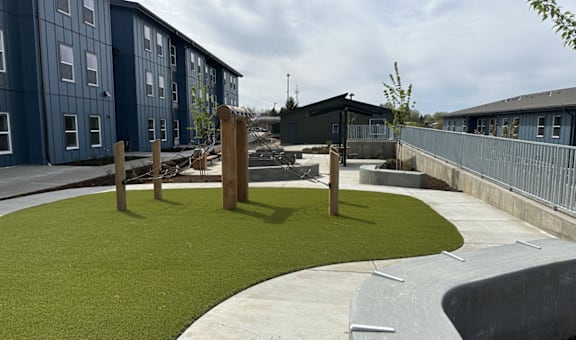 A playground area with artificial grass and a wooden structure in the middle.