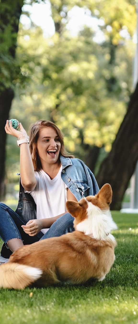  Woman tossing ball to her dog while relaxing in the park.