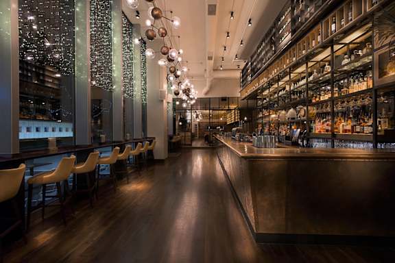 A bar with a long wooden counter and chairs on either side.at Slate Yard Apartments, Salford, M3 5EX