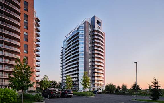 A modern glass building stands next to a red brick building with cars parked in the driveway.