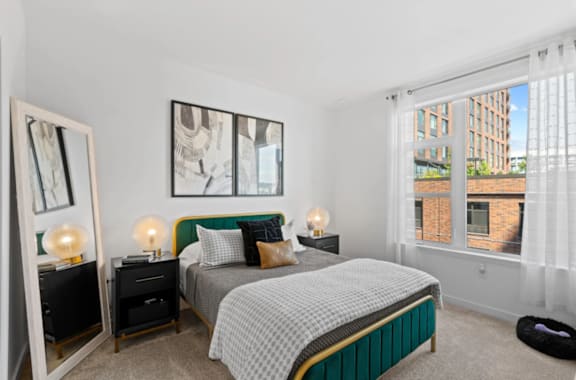 A bedroom with a large bed and a window overlooking a building at The Parker Apartments in Portland, OR 97209