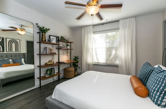A bedroom with a large bed, a ceiling fan, and a mirrored wall.