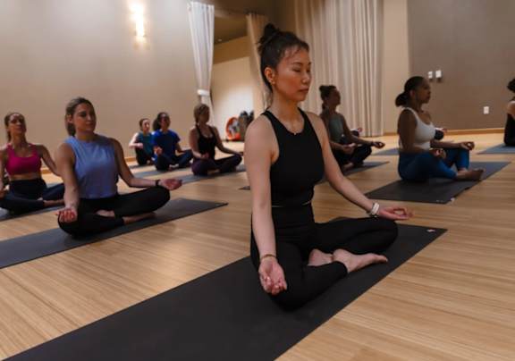 A group of people are sitting on yoga mats in a room.