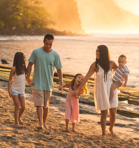 A family of four is walking on the beach at sunset.