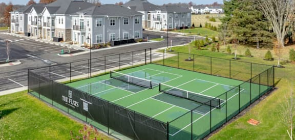 A tennis court is surrounded by a fence and is located in a grassy area.