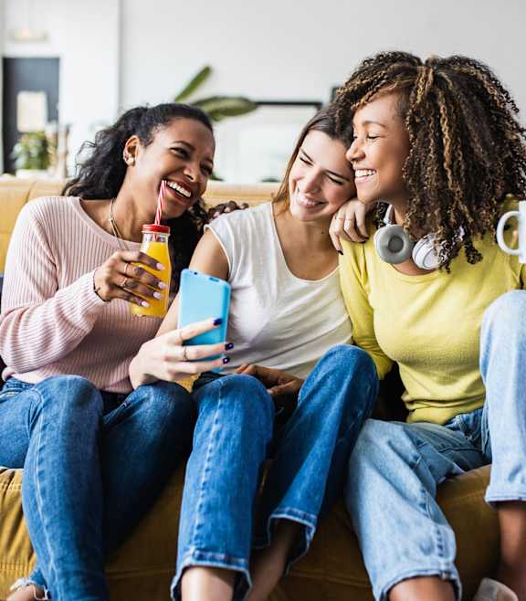 Three friends are sitting on a couch, laughing and enjoying each other's company.