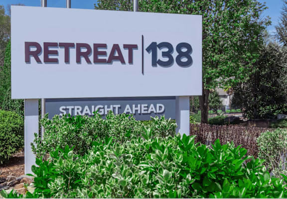 A sign for Retreat 138 Straight Ahead is displayed in front of some greenery.