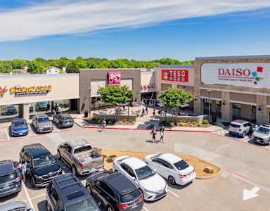 A parking lot with cars and stores in the background.