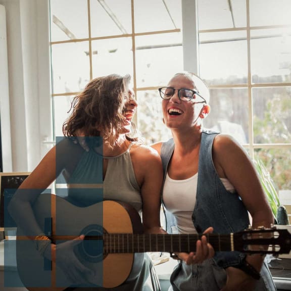two women singing and playing a guitar in a living room
