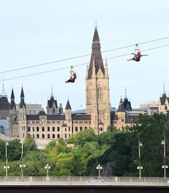 Two people are swinging on a wire in front of a large castle.