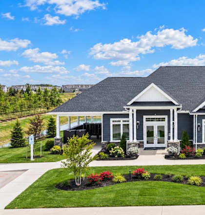 A house with a grey roof and white trim is surrounded by a well-manicured lawn and a variety of plants.