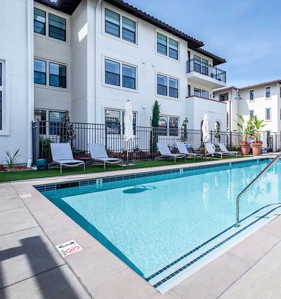 A swimming pool in front of a white apartment building.