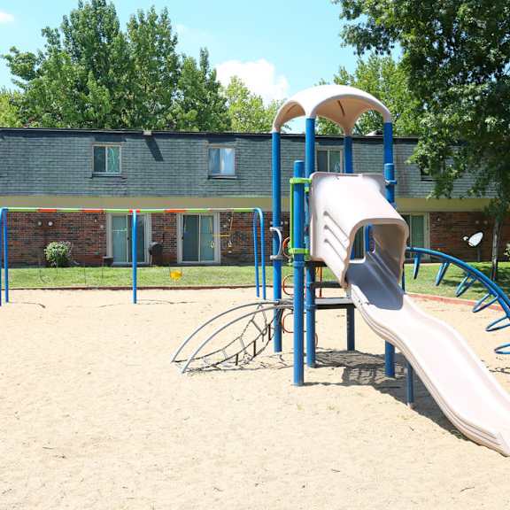 A playground with a slide and a sandbox in front of a building.