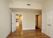 Thumbnail 6 of 23 - A room with white walls and wooden floors, with a door on the right side.