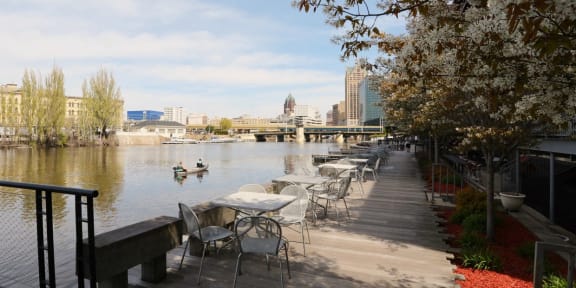 a row of tables and chairs overlooking a river with a city in the background