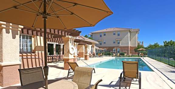 A patio with chairs and an umbrella overlooking a pool.