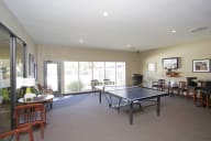 A ping pong table is in the middle of a room with chairs and a television. at The Bridges at Foxridge, Kansas, 66202