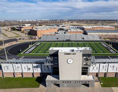 A football field is surrounded by a stadium with bleachers and a scoreboard.