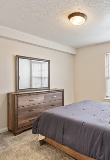 A bedroom with a bed, dresser, and window.