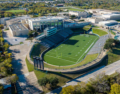 A large stadium with a green field in the center and a building to the left.