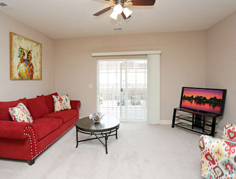 A living room with a red couch, a painting on the wall, and a ceiling fan.