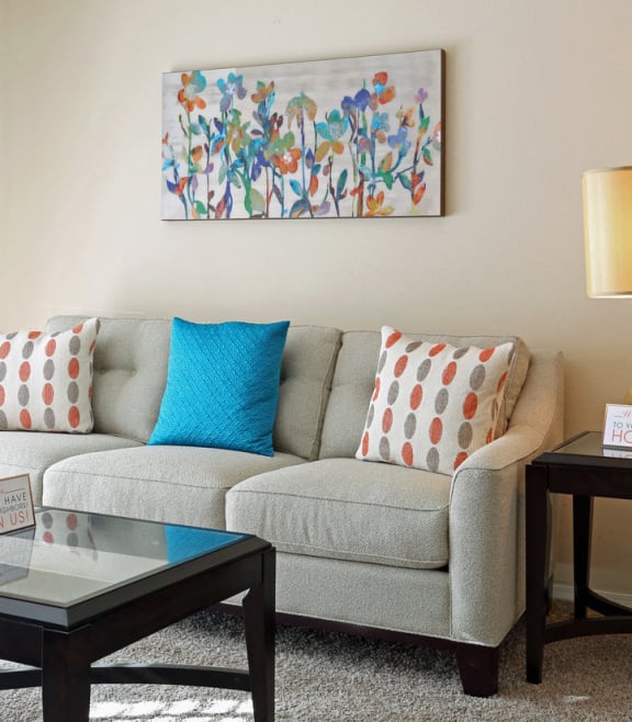 A living room with a grey couch, a glass table, and a painting on the wall. at Champions Club, Glen Allen, 23060