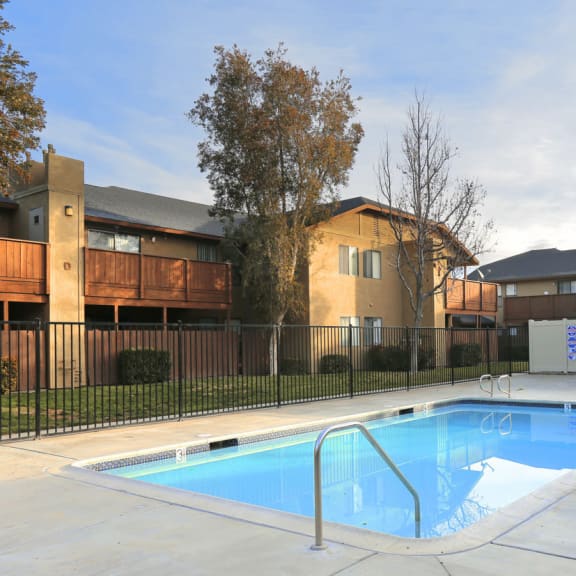 a swimming pool with a fence and apartment buildings in the background