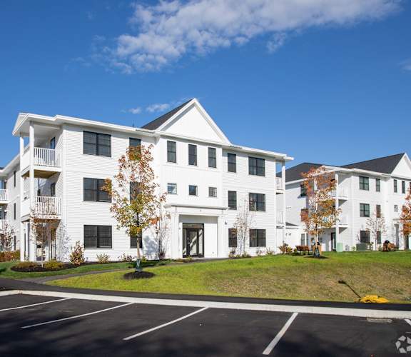 A large white building with a black roof and a parking lot in front.
