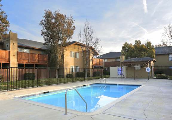 a swimming pool with a fence and apartment buildings in the background