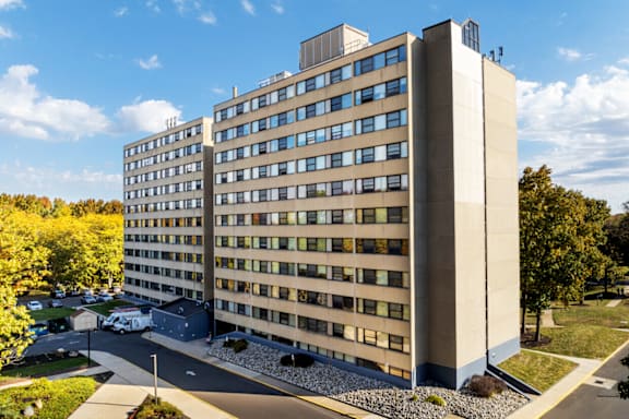 A large beige building with many windows and a parking lot in front.