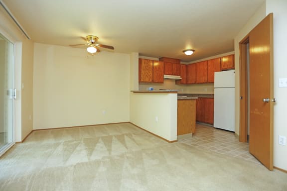 an empty living room with a ceiling fan and a kitchen in the background