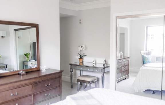 A bedroom with a bed, vanity, and mirror.