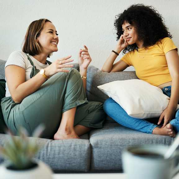 Two women are sitting on a couch having a conversation.