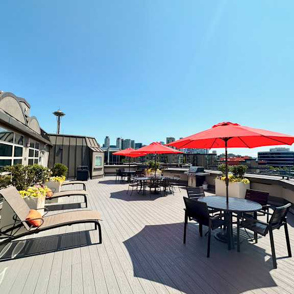 A patio with red umbrellas and chairs overlooking a city skyline.