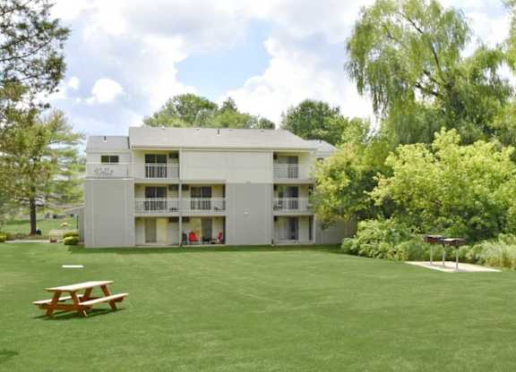 A large white building with a balcony is surrounded by a green lawn.