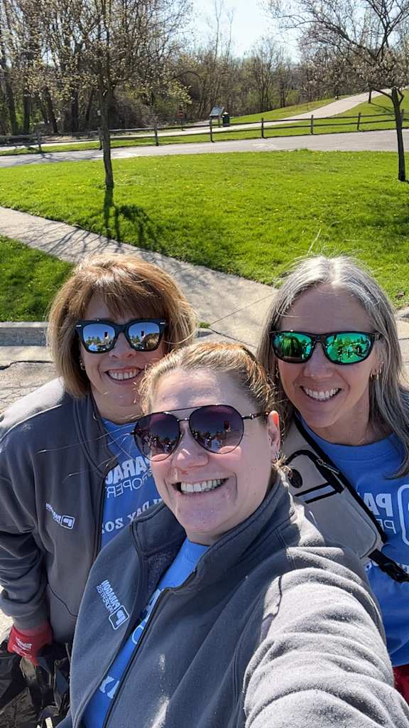Three women wearing sunglasses and blue shirts are taking a selfie.