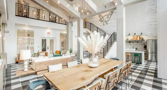Clubhouse great room with a live-edge table, hanging bulbs, a staircase to the loft, and a kitchen with stools.