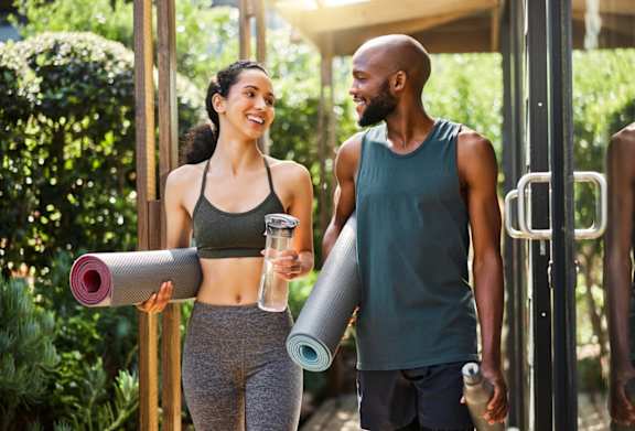 a man and a woman carrying yoga mats in a gym