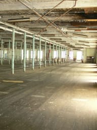 Spacious interior of Converse Mill Lofts before conversion, with green columns, wooden floors, and sunlight streaming through windows.