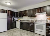 Thumbnail 26 of 28 - A kitchen with white appliances and dark wood cabinets.