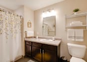 Thumbnail 26 of 27 - A bathroom with a white toilet, a sink, a mirror, and a shower curtain.