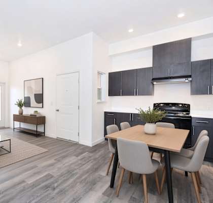 A modern living room with a grey sofa, a coffee table, and a dining table with grey chairs.