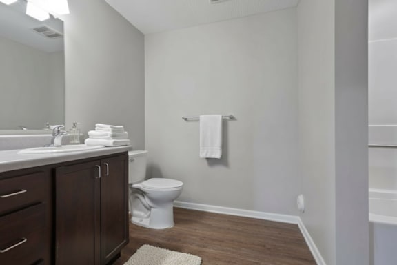 A white toilet sits in a bathroom with a white sink and a white towel hanging on the wall.