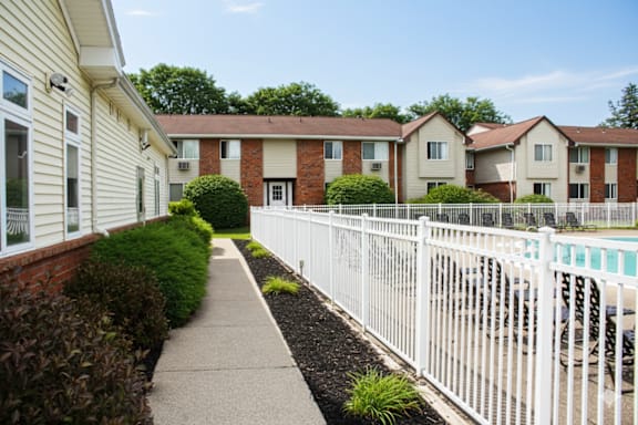 A white picket fence separates a sidewalk from a row of townhouses.