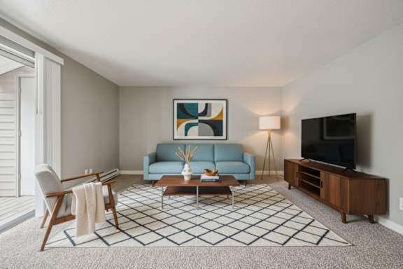A living room with a blue couch, a coffee table, a chair, a painting, a lamp, and a television.