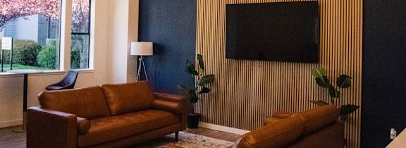 A living room with a brown couch and a flat screen TV mounted on the wall.
