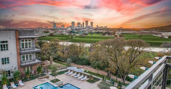 A beautiful sunset view from a balcony overlooking a pool and a city skyline.