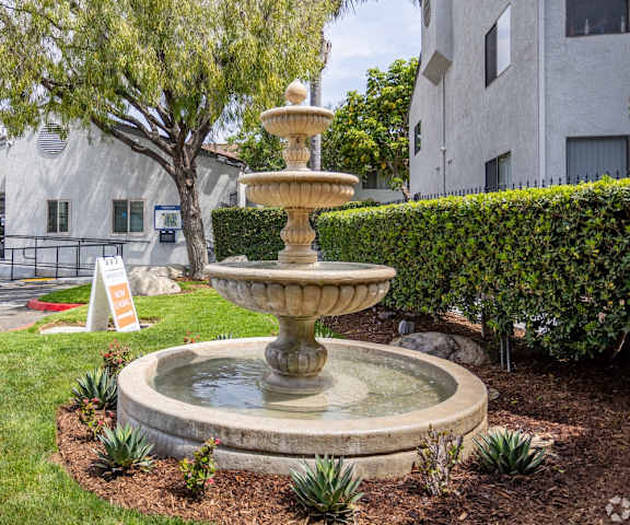 A stone fountain is in the middle of a grassy area.