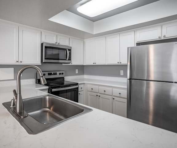 A kitchen with a stainless steel refrigerator, sink, and stove.